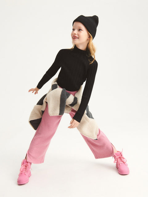 Child wearing a black turtleneck, pink pants, and a patterned coat on a white background
