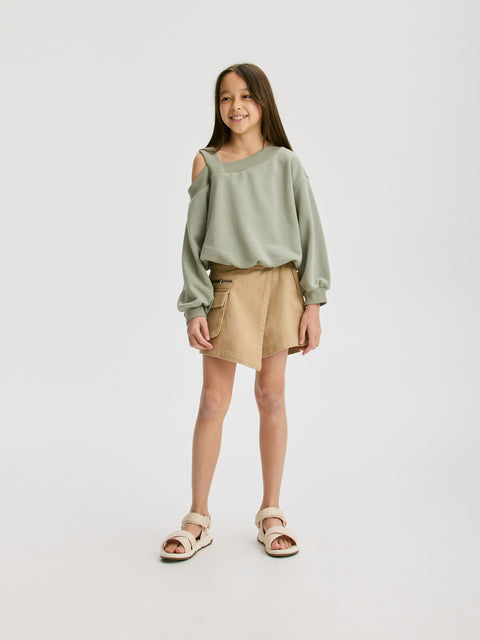 Young girl wearing a green sweater and beige shorts on a white background