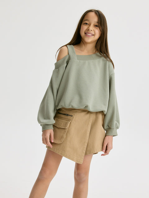 Girl wearing a green sweater and beige skirt on a white background