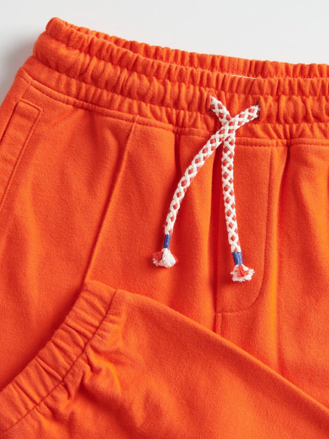 Close-up of orange shorts with a braided drawstring on a light gray background