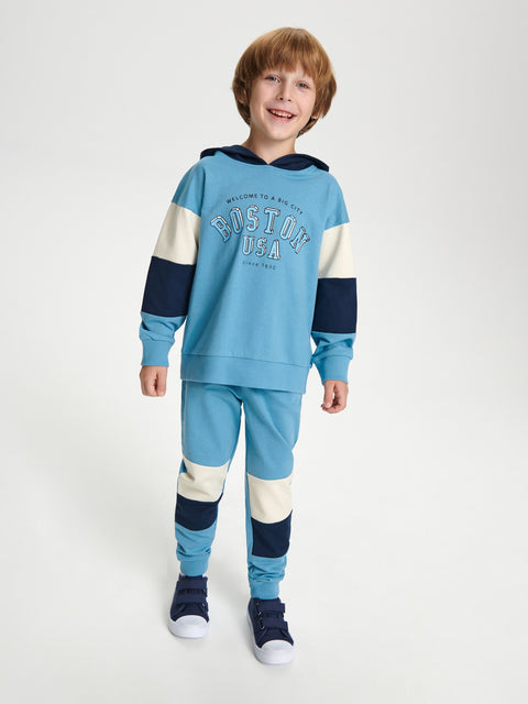 Child wearing a blue and navy tracksuit with 'Boston Tea' text on a white background
