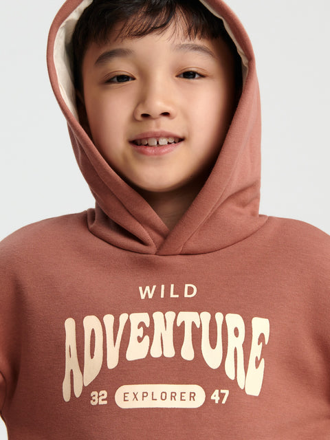 Child wearing a brown hoodie with 'Wild Adventure' text on a plain background