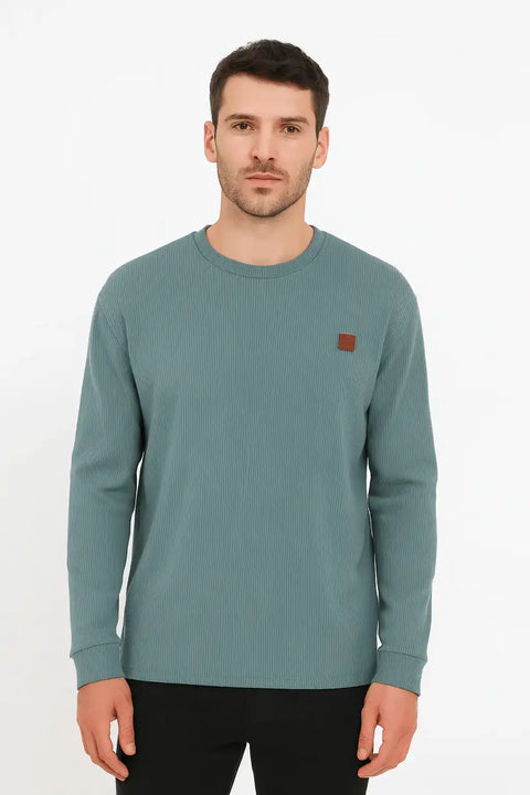 Man wearing a teal long-sleeve shirt with a small brown logo on a white background