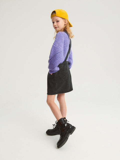 Person wearing a purple sweater, black skirt, and yellow cap on a white background