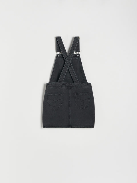Black denim pinafore dress with suspenders on a light gray background