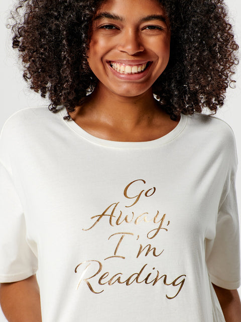 Person wearing a white t-shirt with 'Go Away, I'm Reading' text in gold.