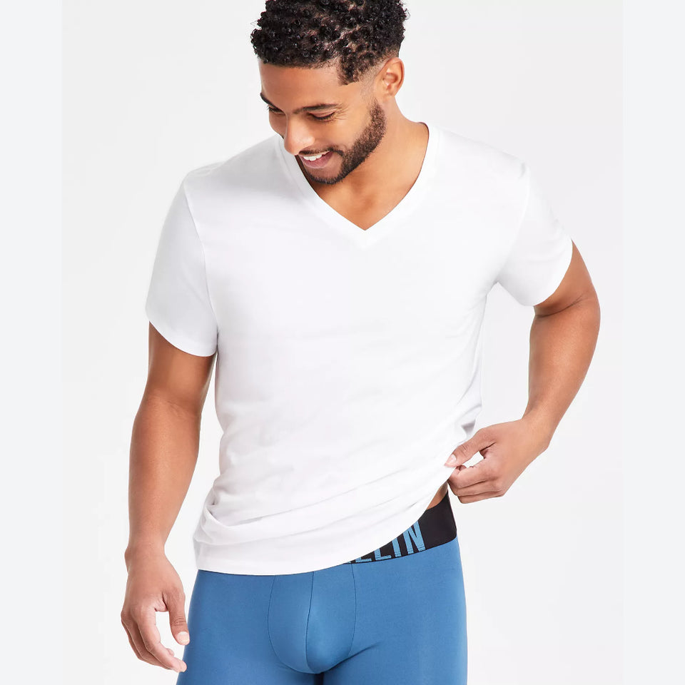 A man wearing a white short-sleeve V-neck t-shirt and blue boxer briefs, shown from the waist up against a light gray studio background.