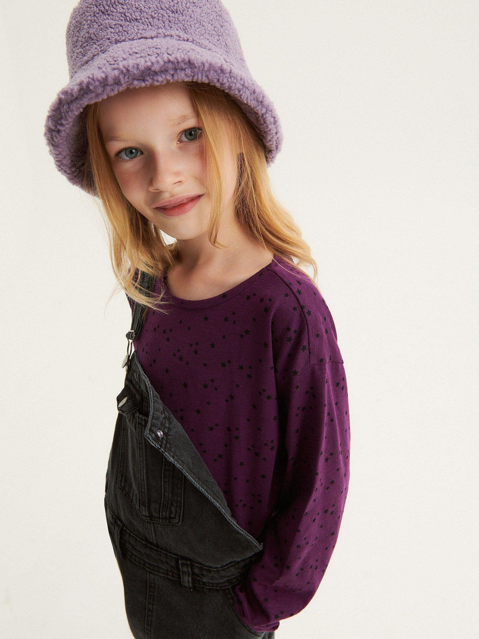 Young girl wearing a purple hat and sweater with a plain background