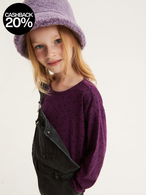 Young girl wearing a purple hat and sweater with a plain background
