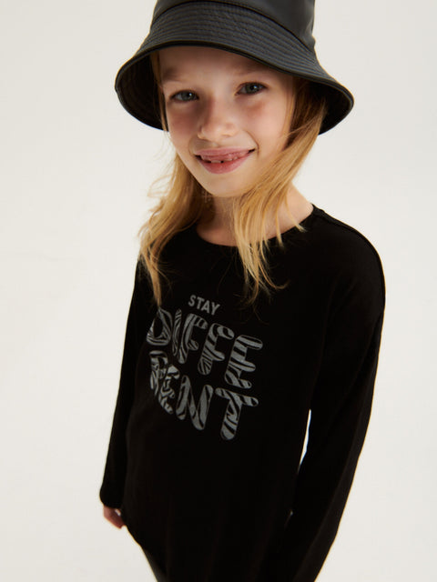 Child wearing a black long-sleeve shirt with text and a black bucket hat on a light gray background