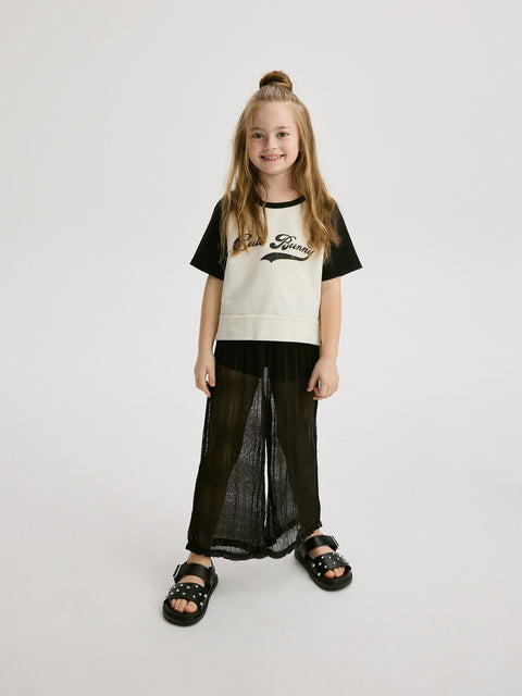 Young girl wearing a black and white t-shirt with text and black pants on a light gray background