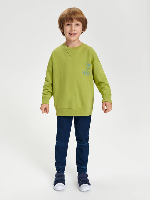 Child wearing a green sweatshirt and blue jeans on a white background
