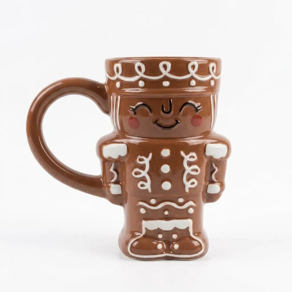 A brown ceramic mug shaped like a gingerbread person, featuring white icing-style details, a smiling face, and a handle on the left side, set against a plain white background.