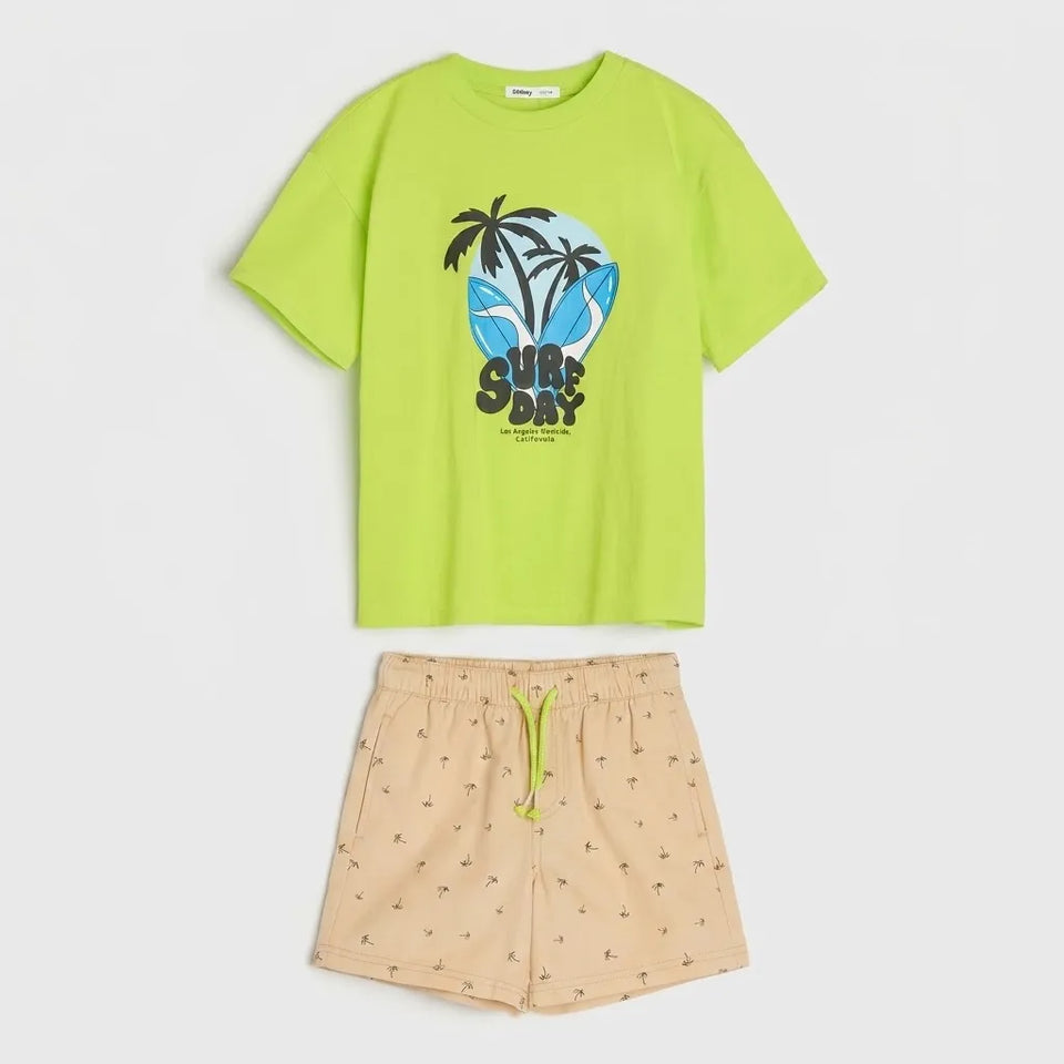 A two-piece kids' outfit set featuring a bright lime green short-sleeve t-shirt with a 'SURF DAY' graphic print, paired with beige shorts patterned with small palm tree silhouettes and a lime green drawstring.