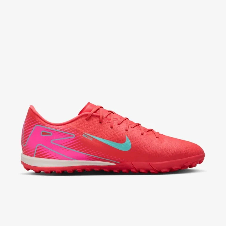 A Nike soccer cleat in bright red with a turquoise swoosh and pink and light blue graphic accents, shown from the side on a light gray background.