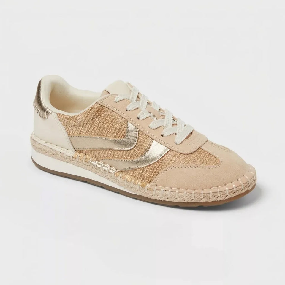A beige and cream espadrille sneaker with metallic gold accents, featuring a woven jute sole and cream laces, shown on a light gray background.