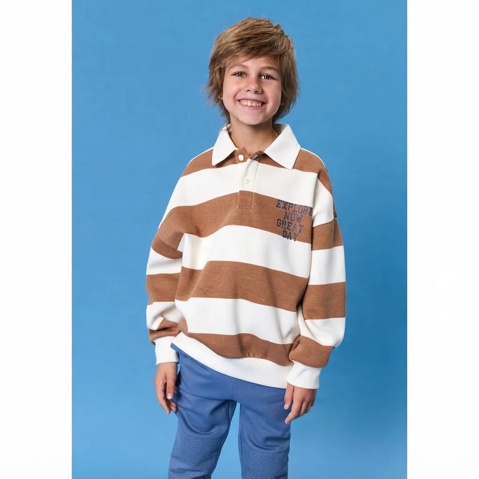 A young boy smiling, wearing a brown and cream horizontally striped long-sleeve rugby shirt with 'EXCUSE ME I'M A DIRT BAY' printed on the chest, paired with blue pants, set against a solid blue background.