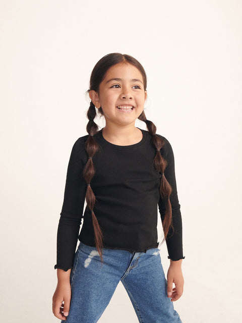 Young girl wearing a black long-sleeve top and blue jeans on a white background