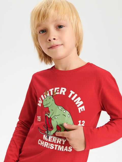 Child wearing a red Christmas-themed shirt with a dinosaur graphic on a plain background