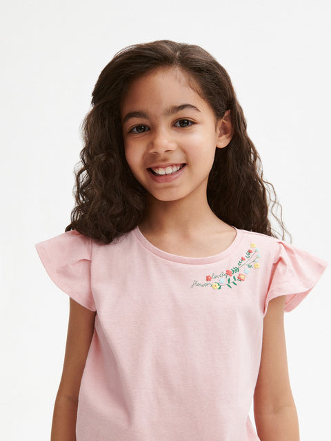 Young girl wearing a pink shirt with floral embroidery on a white background
