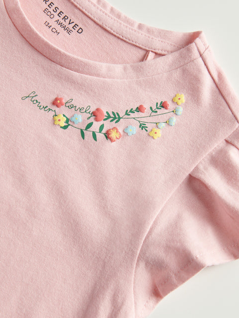 Pink t-shirt with floral embroidery and text on a light background