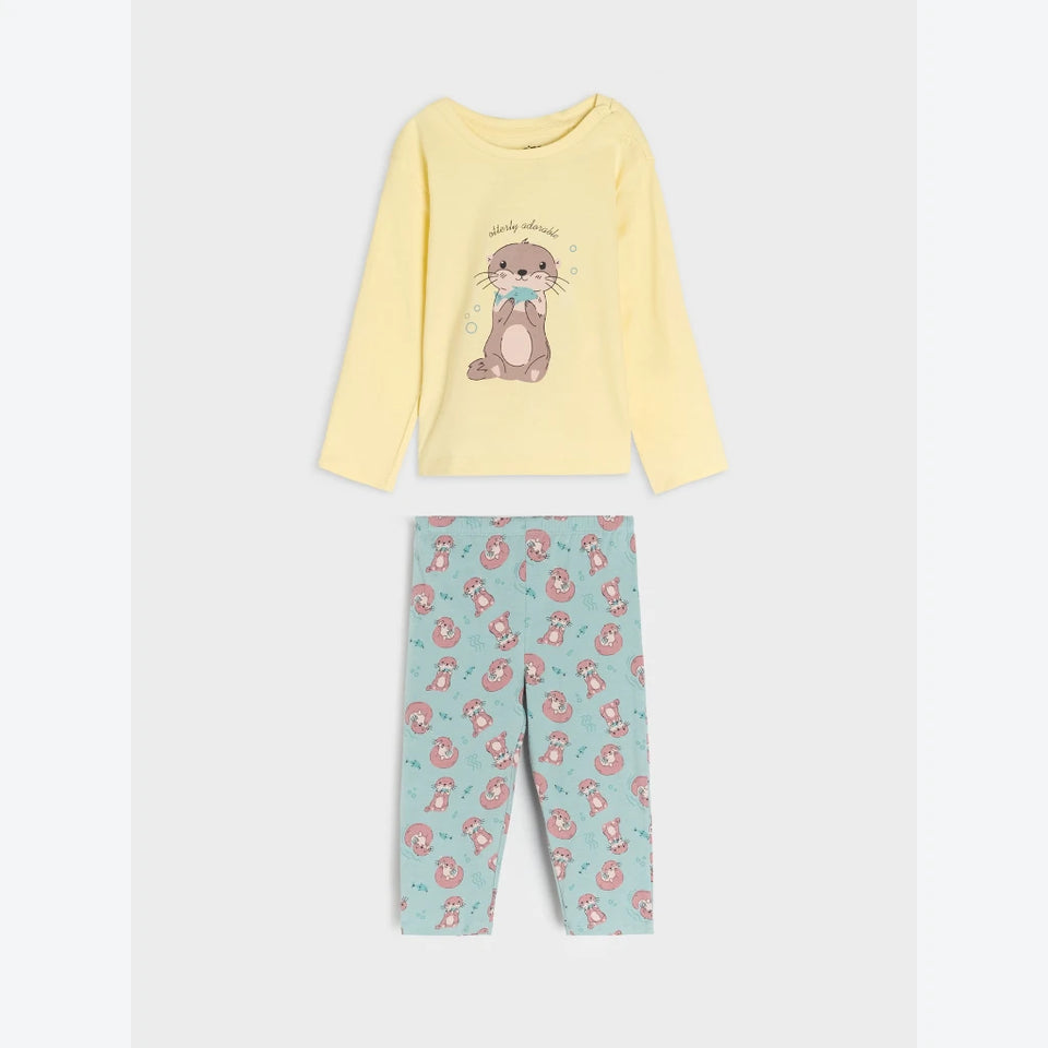 A two-piece children's pajama set featuring a pale yellow long-sleeve top with a cartoon bear graphic and text, paired with light blue pants covered in a pink bear print, displayed on a light gray background.