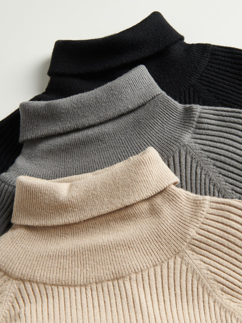 Close-up of three turtleneck sweaters in black, gray, and beige.