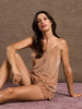 Woman wearing a brown slip dress sitting on a textured surface with a brown background