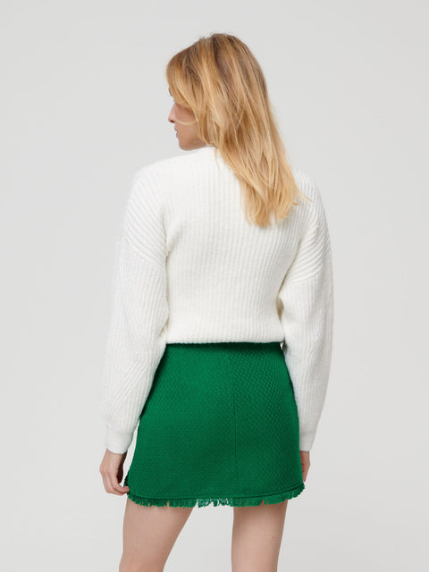 Woman wearing a white sweater and green skirt on a light gray background