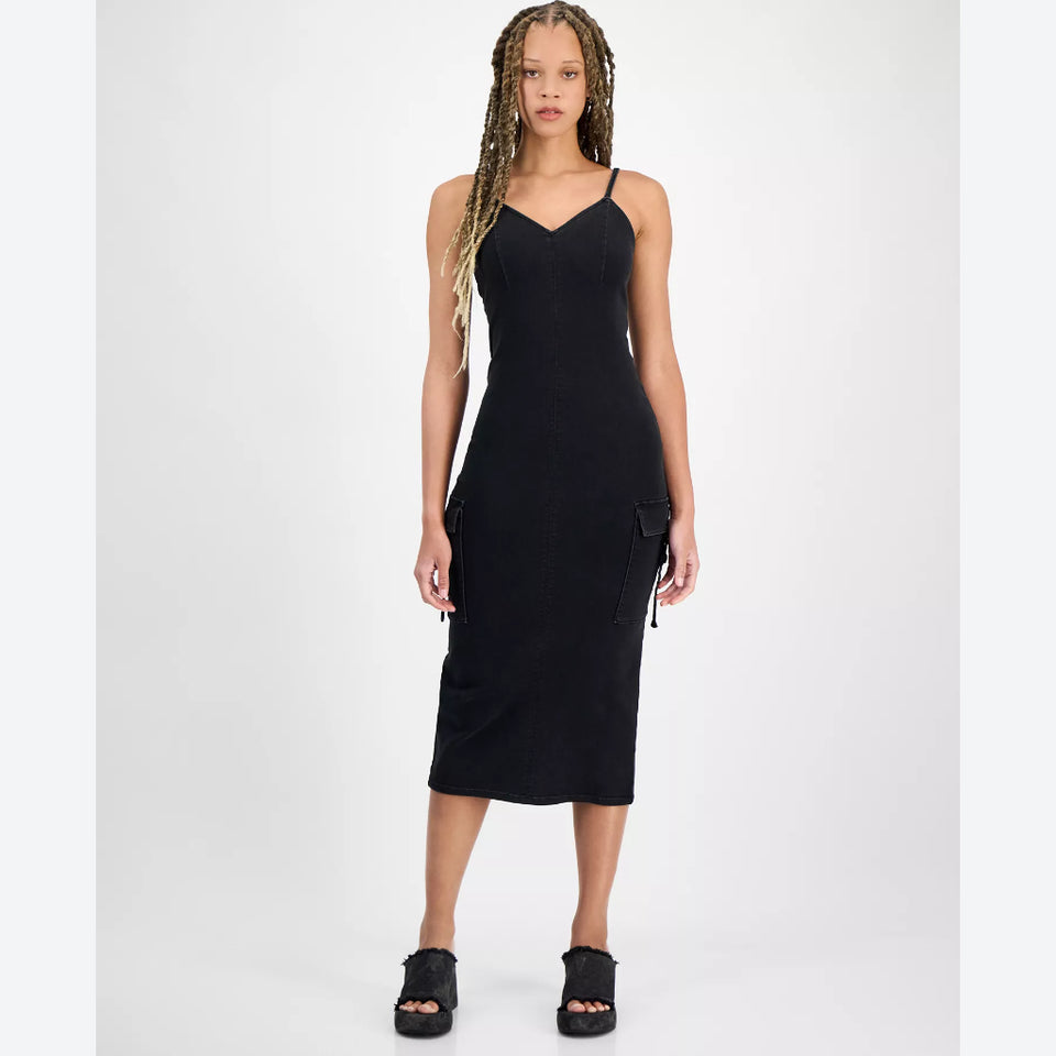 A woman modeling a black spaghetti-strap midi dress with side cargo pockets, paired with black platform sandals, against a plain light gray studio background.