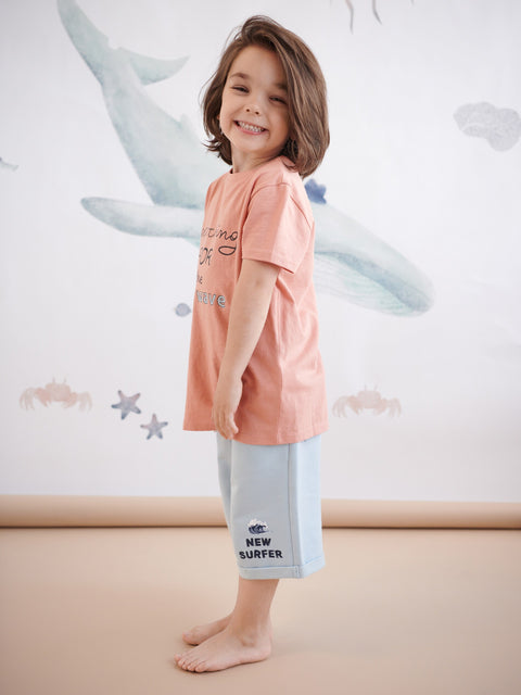 Child wearing a pink shirt and light gray pants with text, standing against a white background with starfish designs.