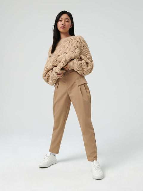 Person wearing a beige cable knit sweater and pants on a white background