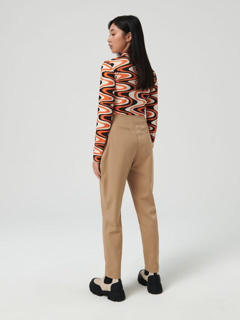 Woman wearing a patterned top and beige pants on a white background