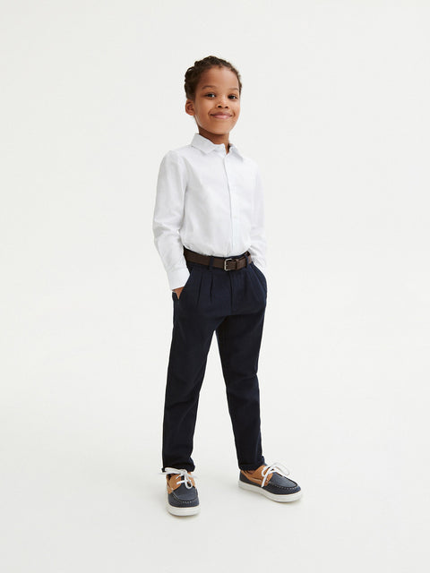 Child wearing a white shirt, navy pants, and black shoes on a white background