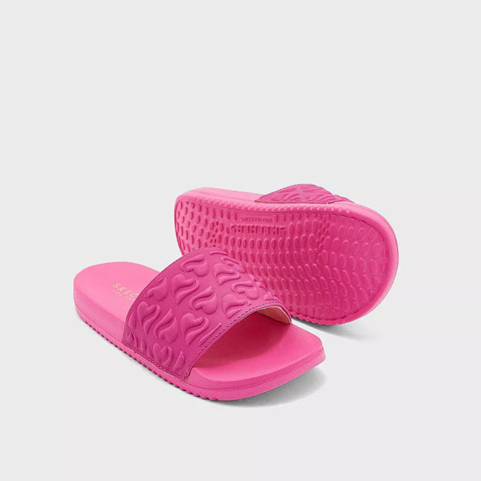 A pair of bright pink slide sandals with textured wavy straps and a raised wavy sole, shown on a light gray background.