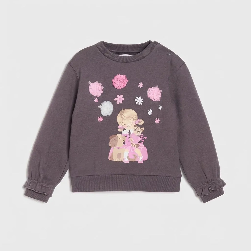 A dark gray long-sleeve sweatshirt for toddlers, featuring a cute cartoon girl and dog graphic on the front surrounded by pink and white pom-poms and flowers. The sweatshirt has gathered cuffs and a ribbed crew neck, hem, and sleeves.