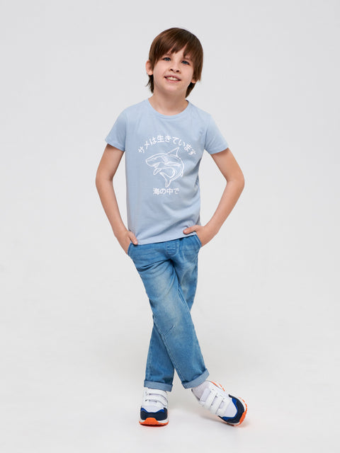 Child wearing a light blue t-shirt with a graphic design and blue jeans on a white background