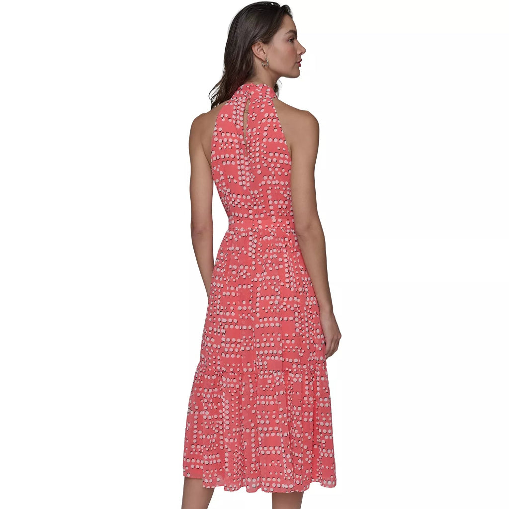 A woman modeling a sleeveless halter-neck midi dress with a coral pink and white geometric pattern, shown from the back against a plain white background.