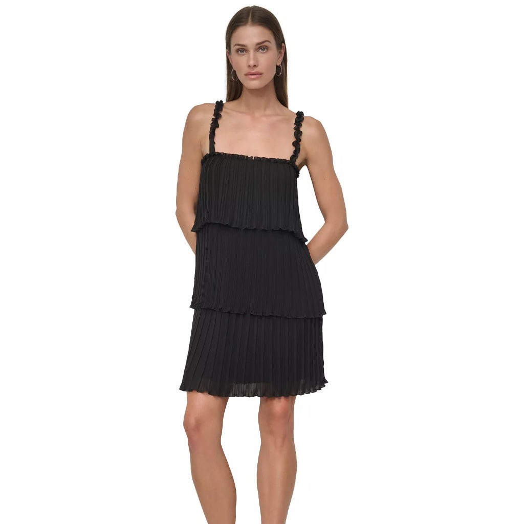 A woman modeling a black pleated tiered mini dress with ruffled shoulder straps, paired with black pointed-toe heels, against a plain white background.