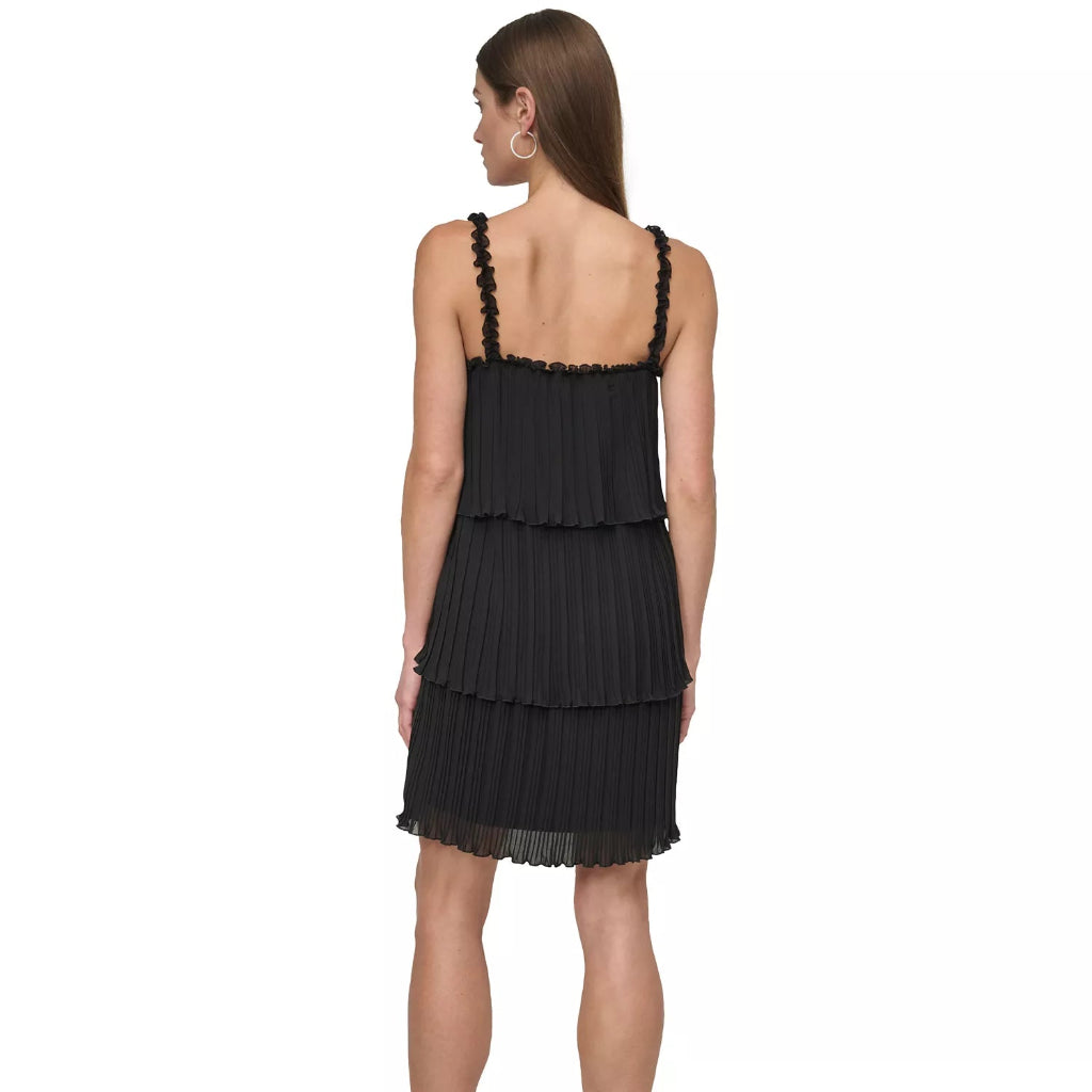 A woman shown from the back wearing a black pleated tiered mini dress with ruffled shoulder straps, paired with black pointed-toe heels, against a plain white background.