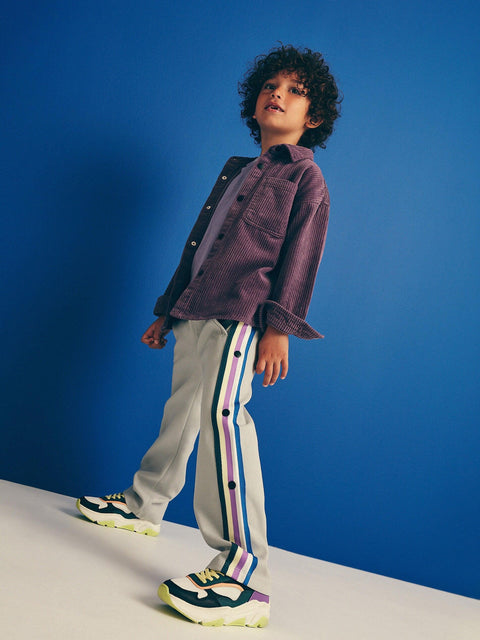 Child wearing a purple shirt and gray pants with colorful stripes against a blue background