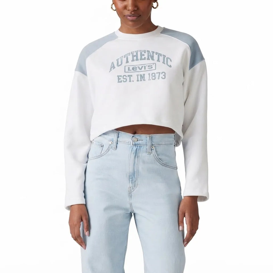 A model wearing a white and light gray color-blocked Levi's crop sweatshirt with a gray graphic print on the front, paired with light-wash blue jeans, against a plain white background.