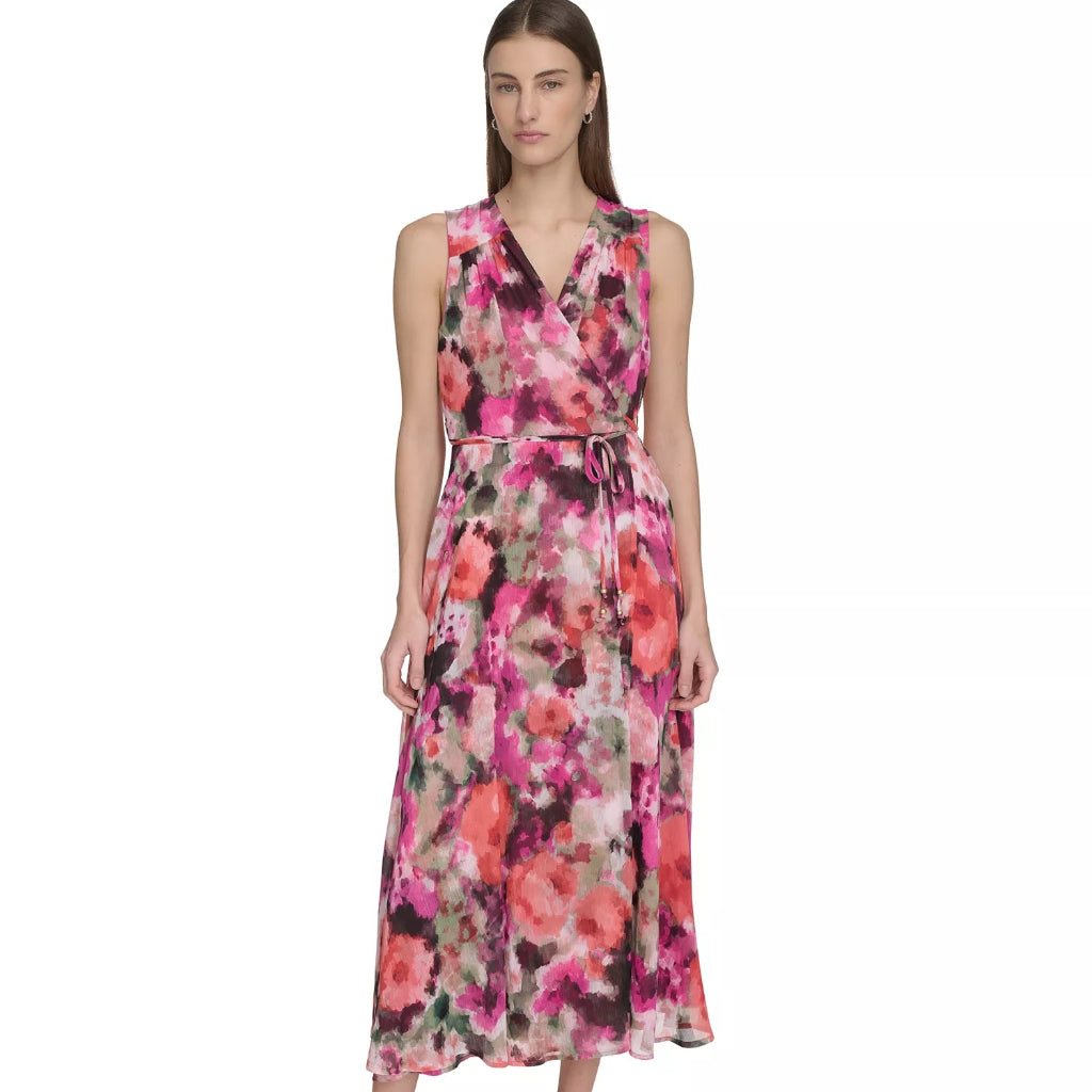 A woman modeling a sleeveless midi wrap dress with a vibrant pink, red, and purple floral print on a light background, paired with nude heels, set against a plain white studio background.