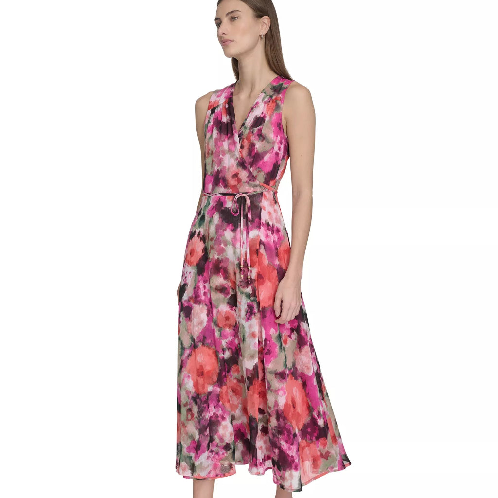 A woman modeling a sleeveless midi dress with a vibrant pink, red, and orange floral print on a white base, paired with nude high heels against a plain white background.