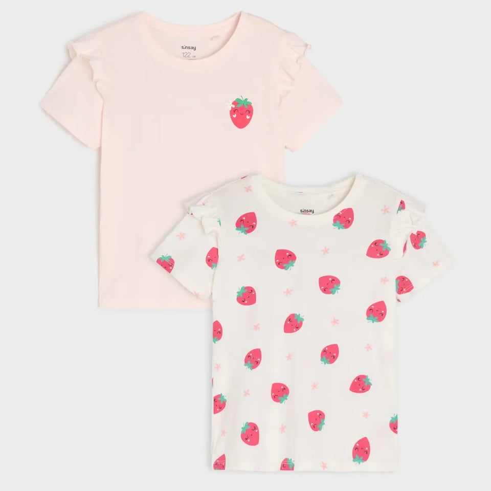 Two children's short-sleeve ruffle-edge T-shirts laid flat on a light gray background. The top shirt is pale pink with a small strawberry graphic on the chest.