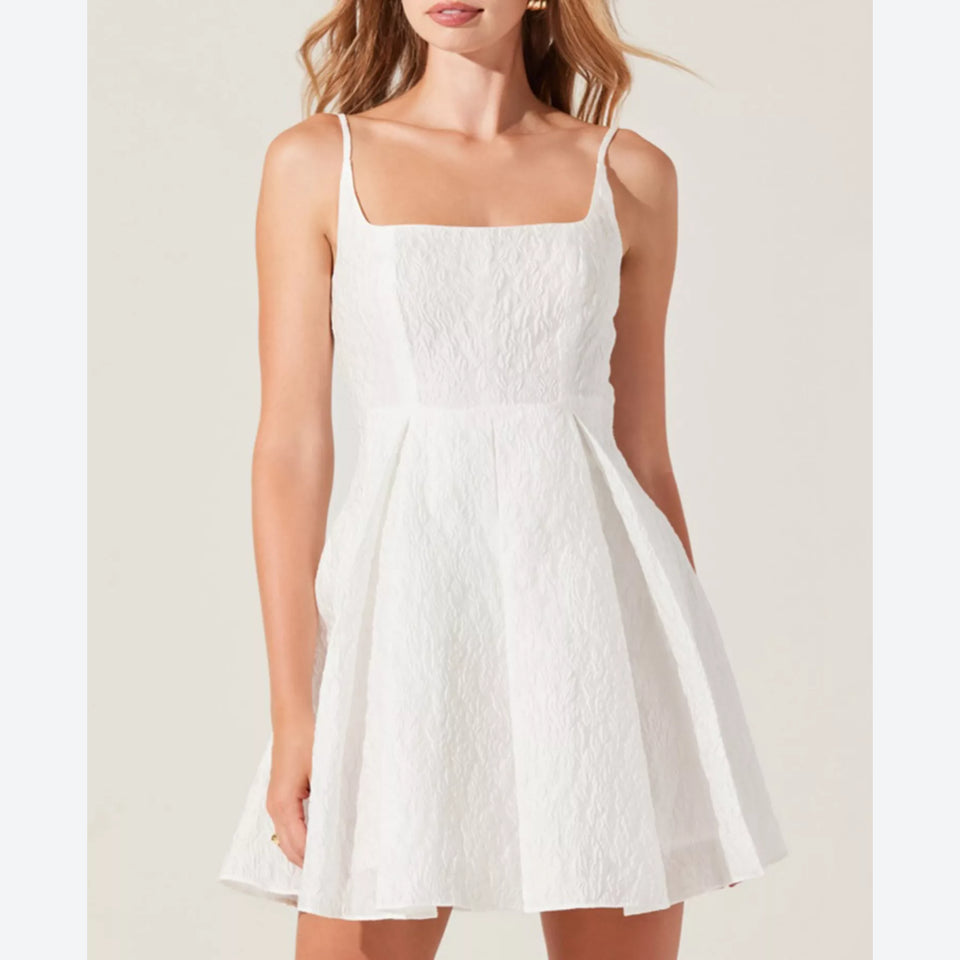 A woman wearing a white textured spaghetti-strap mini dress with a square neckline and a flared skirt, shown against a plain light beige background.