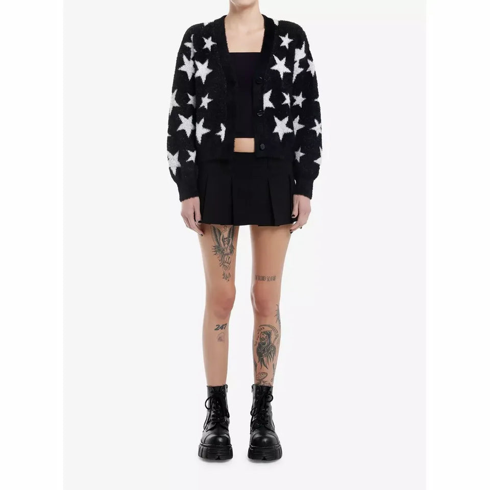 A model wearing a black cardigan with a white star pattern, a black pleated mini skirt, a black top, and black combat boots, shown against a plain white studio background.