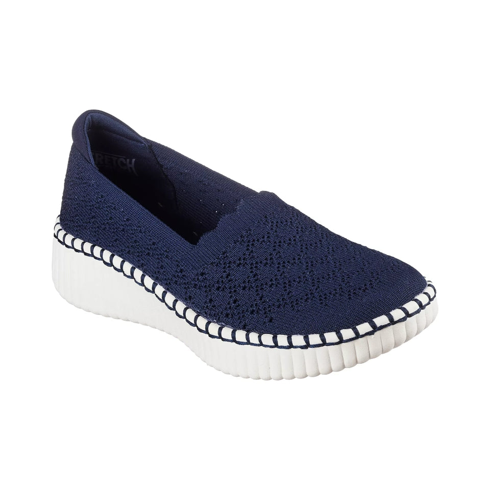 A navy blue knit slip-on shoe with a white textured sole and white stitching along the edge, shown against a plain white background.
