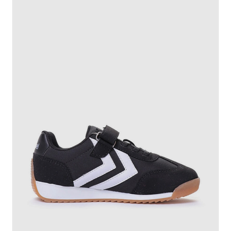 A black and white low-top sneaker with a hook-and-loop strap closure and a gum rubber sole, shown from a side profile on a light gray background.