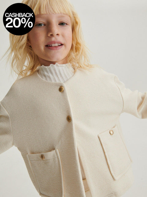 Child wearing a cream-colored cardigan with buttons on a plain background